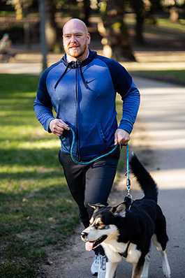 careoregon_kris_feb2025_fj6a3944_jasonquigley-story A man in a blue sweatshirt runs in the park with his dog