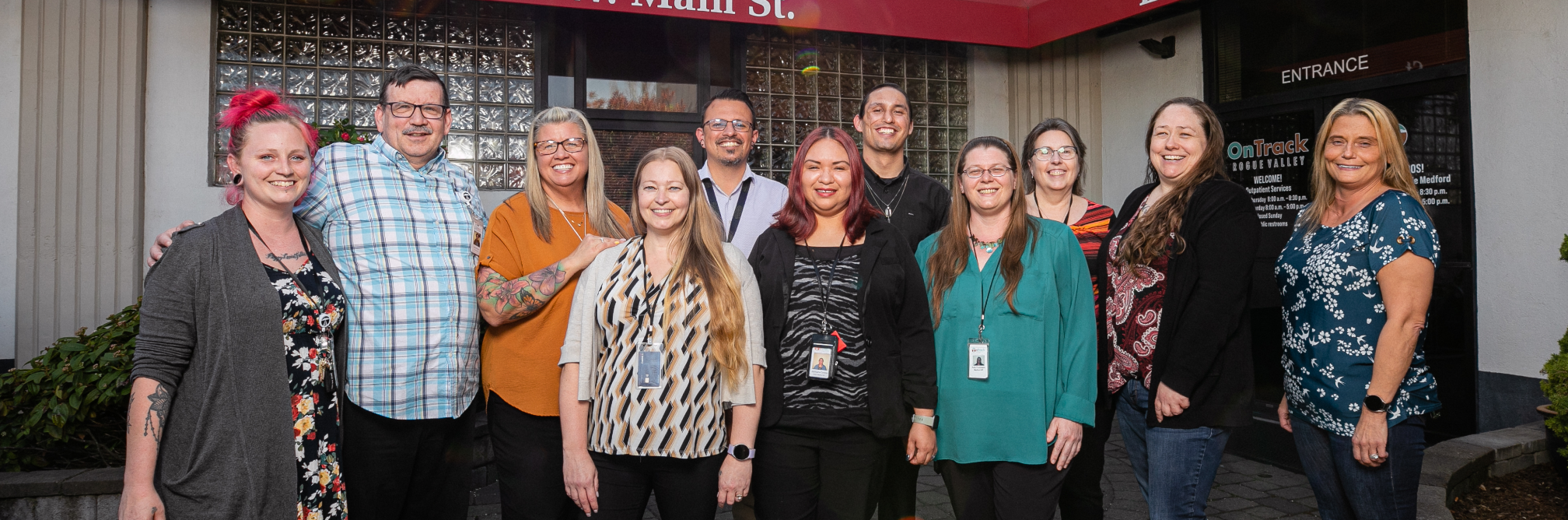 Eleven adults in casual business attire stand smiling at the entrance to OnTrack Rogue Valley, a treatment center that received additional staff funding from CareOregon.