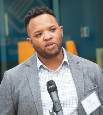 Jeremiah Rigsby, Chief of Staff at CareOregon, stands before a microphone at an outdoor event at the CareOregon Boys & Girls Club at Rockwood.