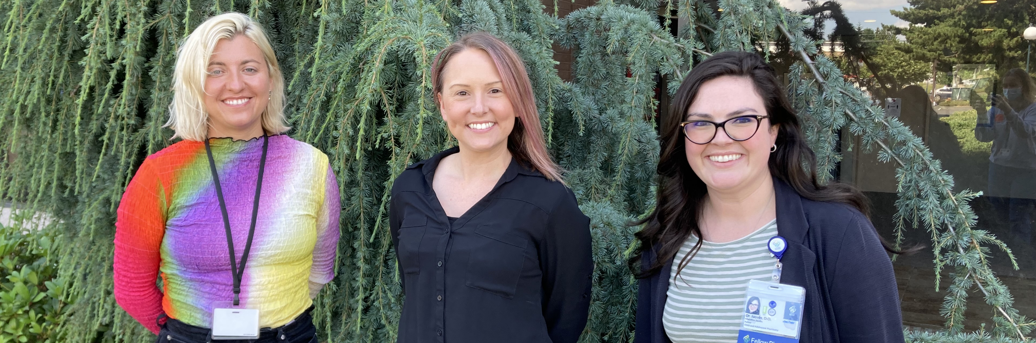 Three female clinicians -- part of the Bridge Clinic team of child mental health professionals -- smile as they stand together in front of landscaped area on the OHSU campus.