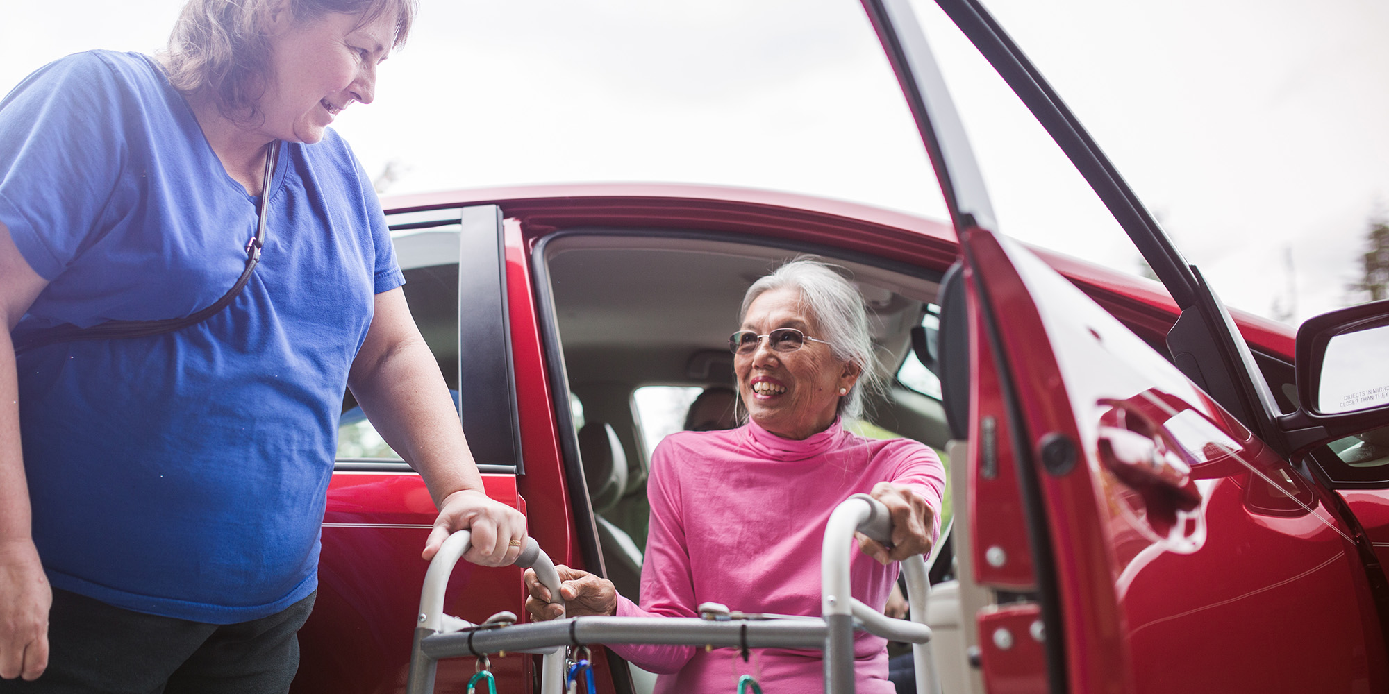 Woman wearing pink gets out of a car using a walker
