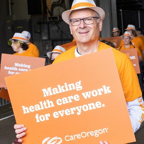 careoregon-mission 1 一群身穿橙色服装的人在游行中举着标语,上面写着“Making health care work for everyone. CareOregon”。