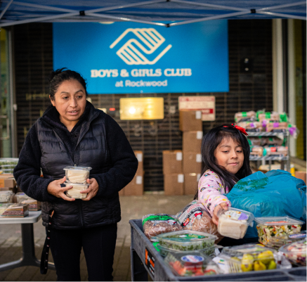 Person and child in front of a table full of food items at the CareOregon Boys & Girls Club at Rockwood. 
