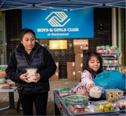 Mujer y niña delante de una mesa llena de productos alimenticios en CareOregon Boys & Girls Club en Rockwood.