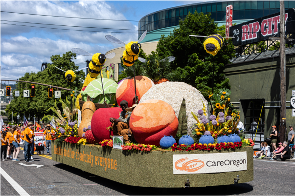 Una carroza colorida adornada con grandes flores y abejas, patrocinada por CareOregon, durante un desfile a pleno sol
