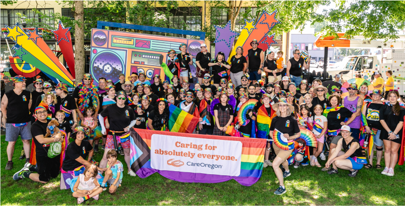 A group of people at a pride event, holding a banner that says ‘Caring for absolutely everyone’ with a CareOregon logo 