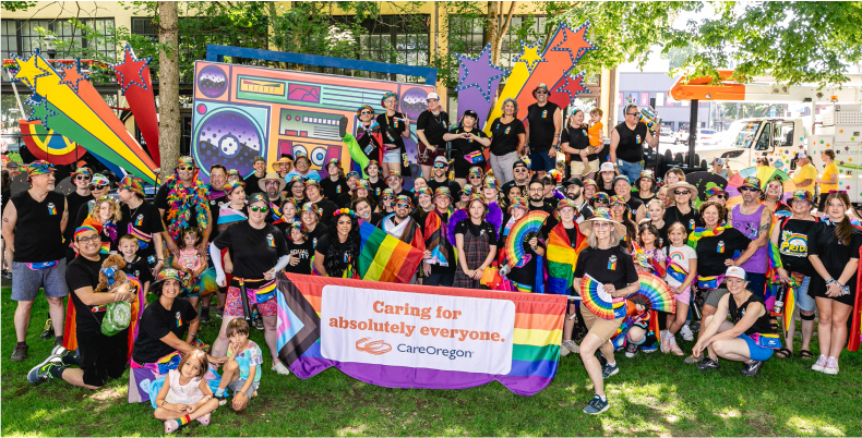 Un grupo de personas reunidas en un evento del orgullo sostienen un banner que dice: "Cuidamos de absolutamente todos" con el logotipo de CareOregon