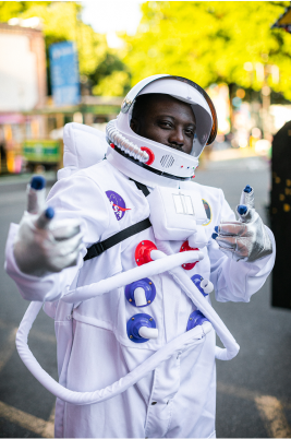 Una persona disfrazada de astronauta parada en la calle de una ciudad con el rostro oculto y un fondo de árboles borroso