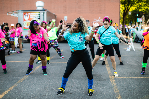 Un grupo de personas con prendas coloridas bailan en la calle durante un evento público, en una atmósfera festiva
