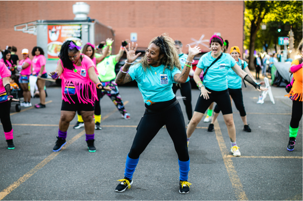 A group of people in colorful attire dancing on a street during a public event, with a festive atmosphere 