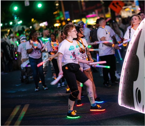 A group of people wearing colorful attire and light-up shoes, participating in a nighttime parade. 