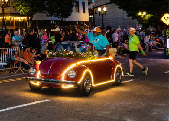 一辆装饰着灯光的老式红色汽车参加夜间游行，周围环绕着观众