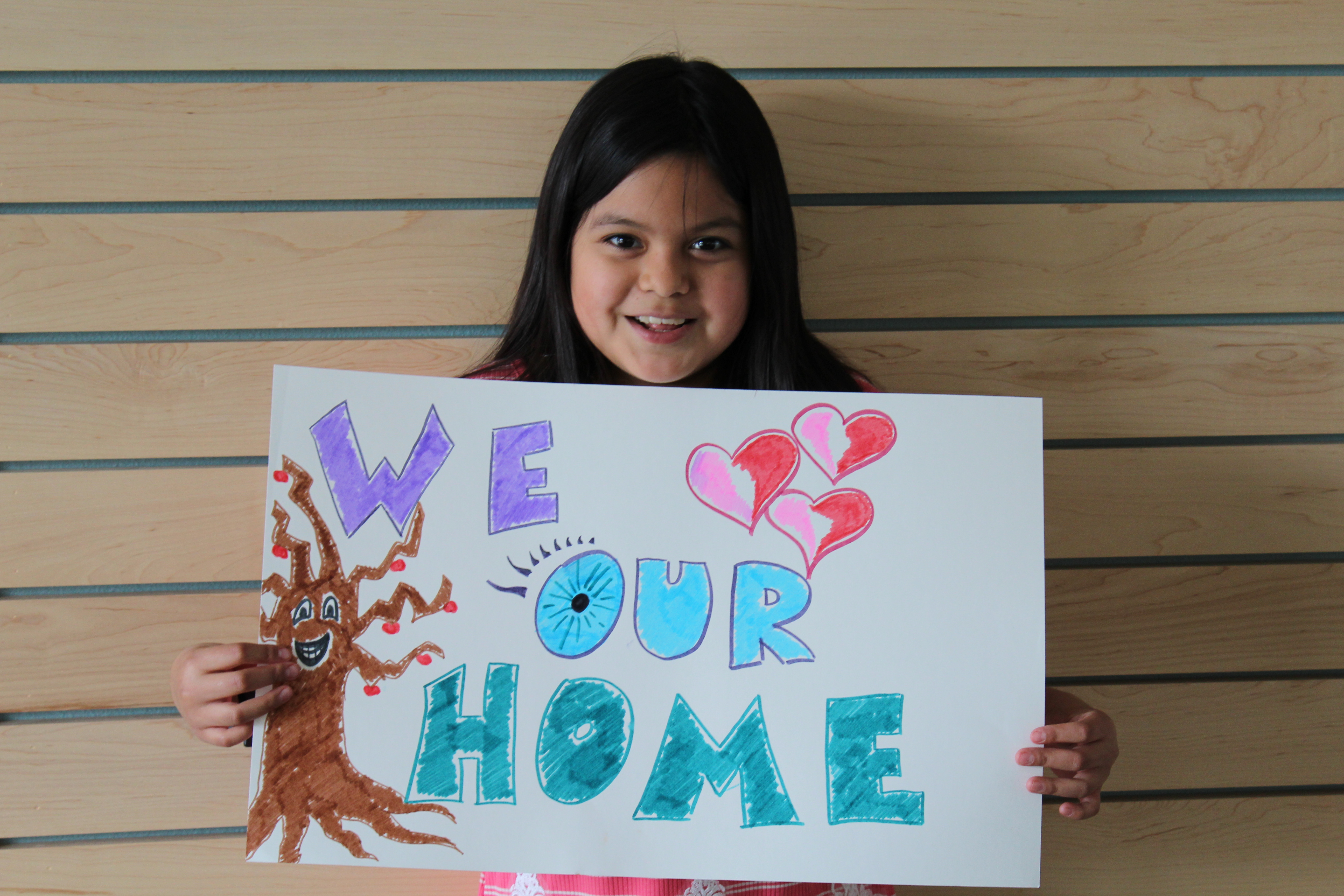 Niño sosteniendo un cartel que dice "amamos nuestra casa".