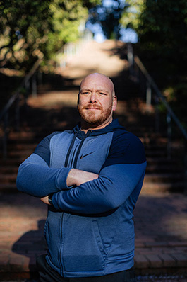 careoregon_kris_feb2025_fj6a3986_jasonquigley-story A man in a blue sweatshrit stands with his arms crossed looking at the camera