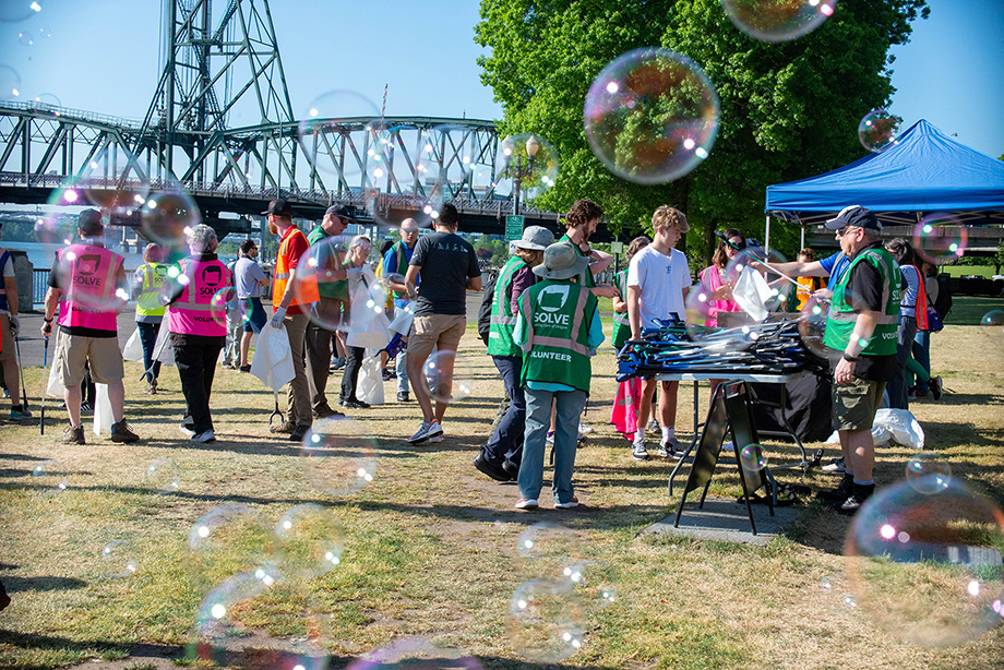 Một nhóm người tham gia dọn dẹp dọc bờ sông Portland, với một cây cầu ở hậu cảnh và bong bóng ở tiền cảnh.